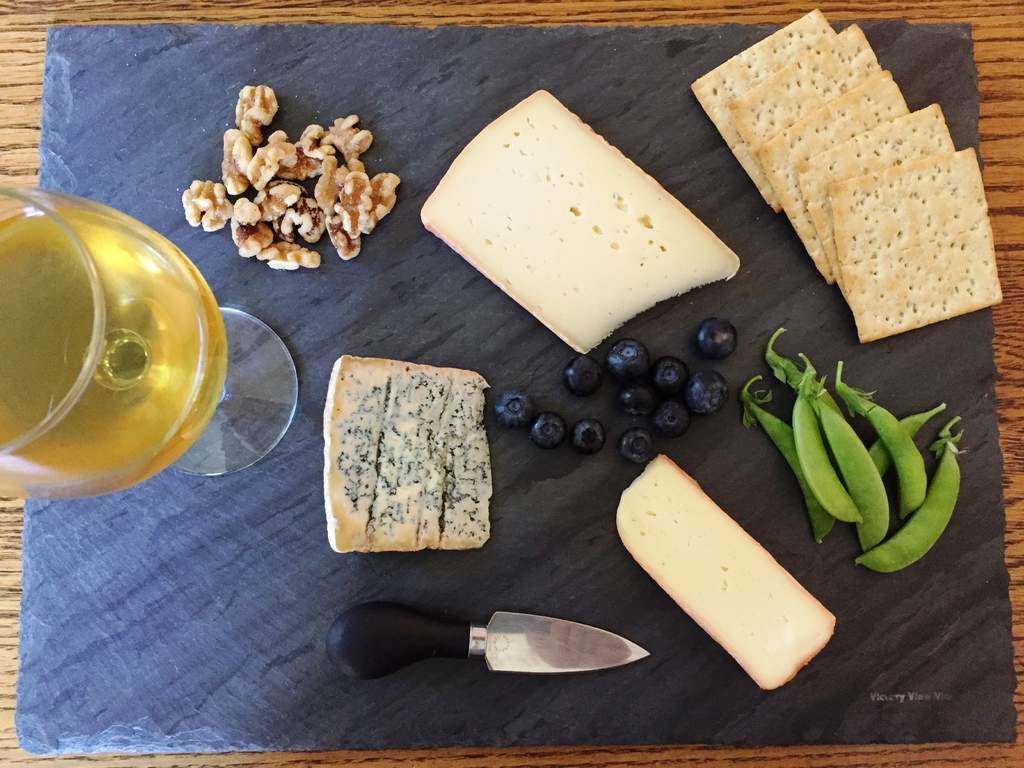 wine and cheese 3 cheese wedges on slate with crackers, berries, nuts
